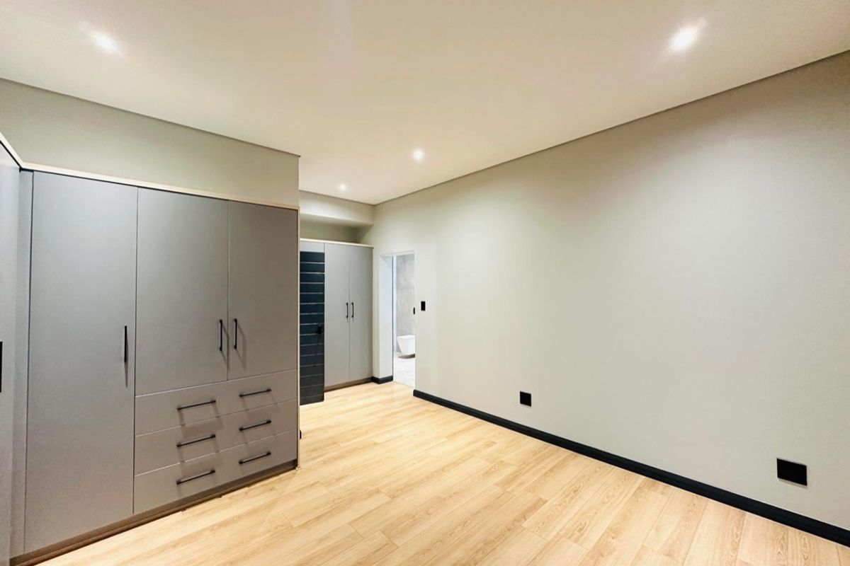 A modern, empty bedroom featuring light wood-look laminate flooring, neutral walls, recessed lighting, and extensive built-in cabinetry with dark hardware.