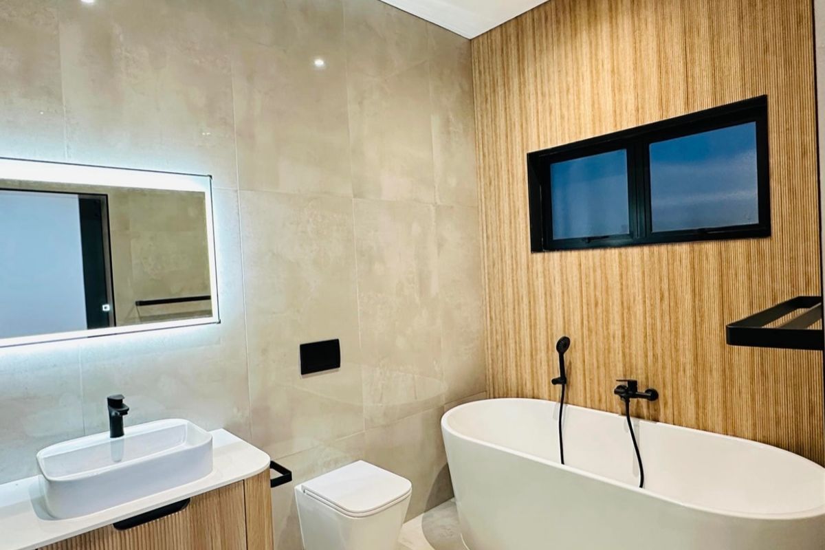 Modern bathroom featuring a freestanding bathtub, wall-mounted toilet, vessel sink on a timber-look vanity, and stylish black matte fixtures with ambient lighting.