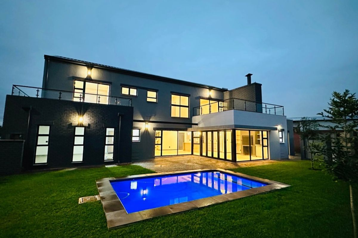Modern double-story rear elevation featuring a swimming pool, expansive glass bi-fold doors, and a balcony with glass balustrades, set against a landscaped garden.
