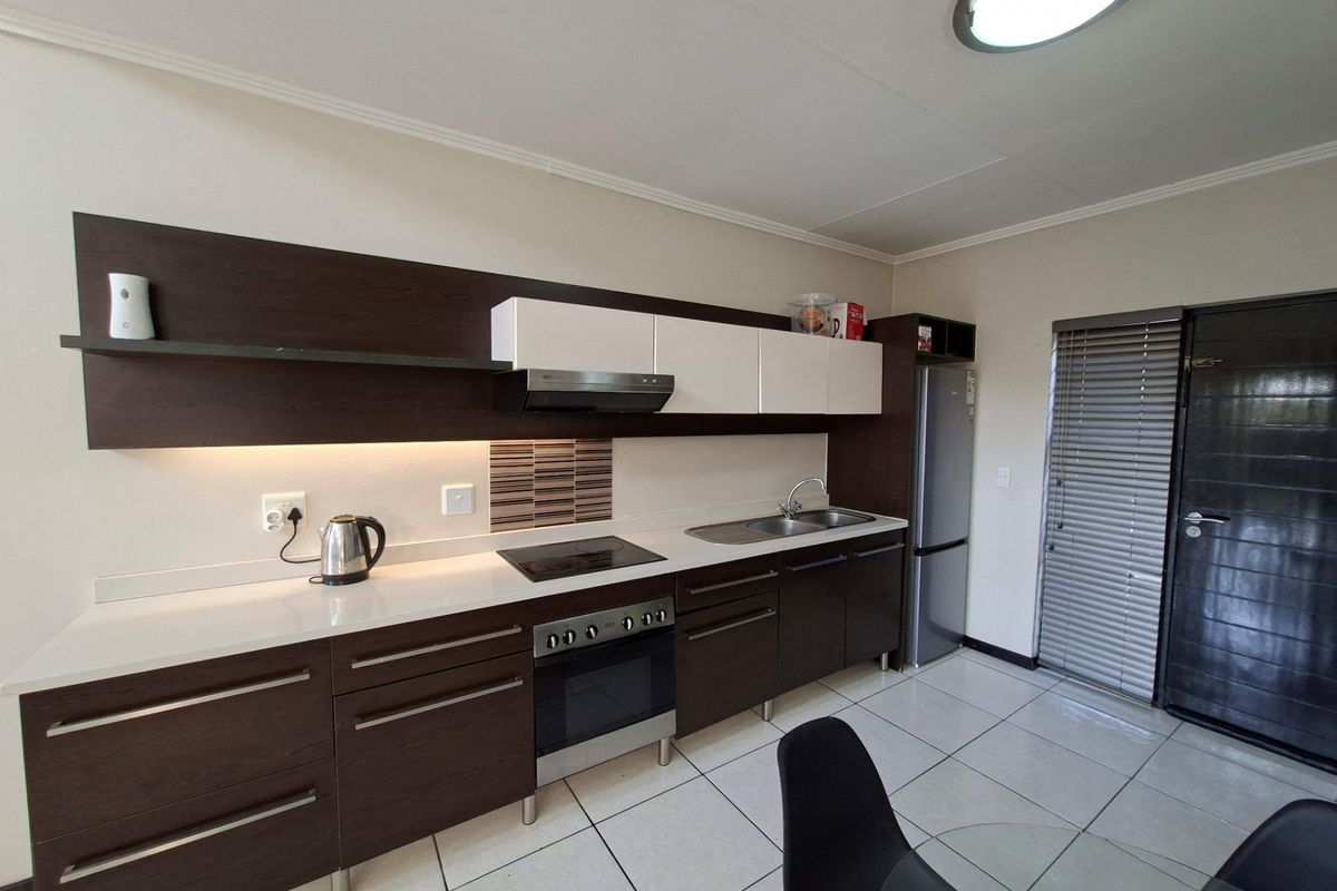 Modern kitchen featuring dark wood and white cabinetry, integrated electric hob and oven, stainless steel sink, and tiled flooring with under-cabinet lighting.