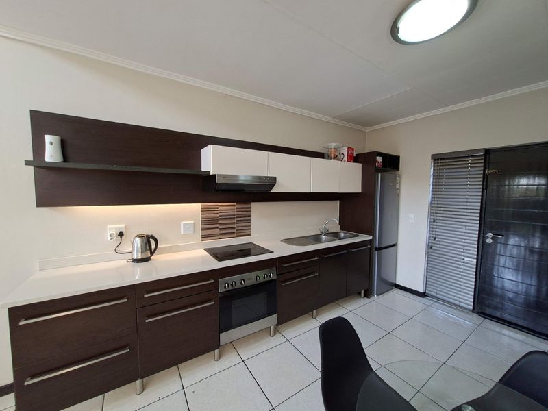 Modern kitchen featuring dark wood and white cabinetry, integrated electric hob and oven, stainless steel sink, and tiled flooring with under-cabinet lighting.