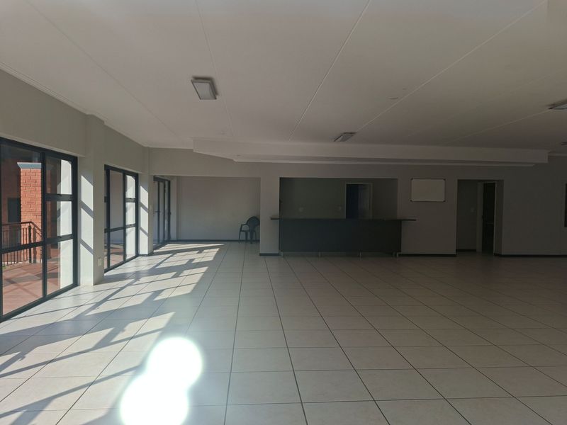 Spacious open-plan area featuring tiled flooring, a built-in bar counter, and large windows providing ample natural light, suitable for versatile living or entertainment use.