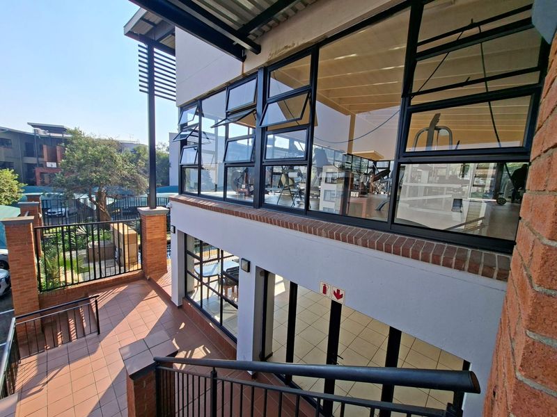 Exterior view of a multi-level apartment complex featuring a tiled patio, metal staircase, and large glass windows overlooking the communal area.