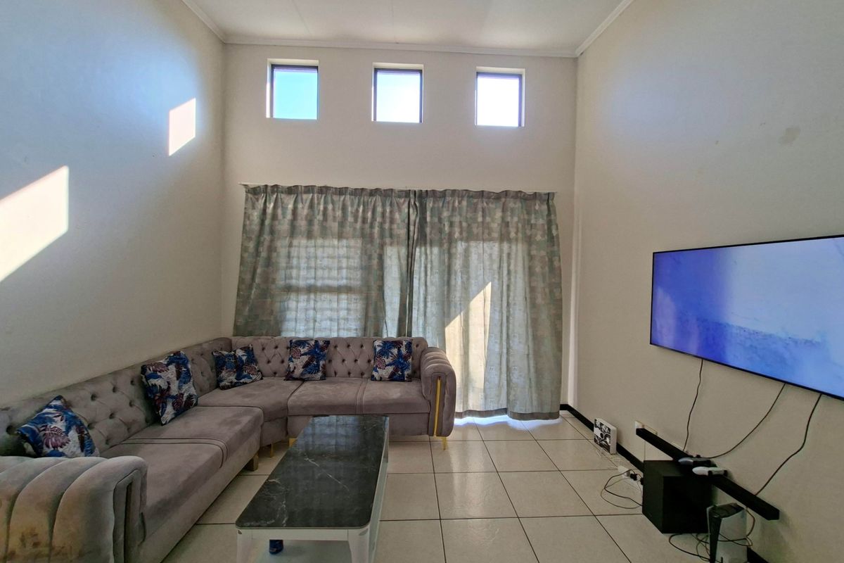 Spacious living room featuring high ceilings, clerestory windows, tiled flooring, and a sliding glass door providing access to the exterior.