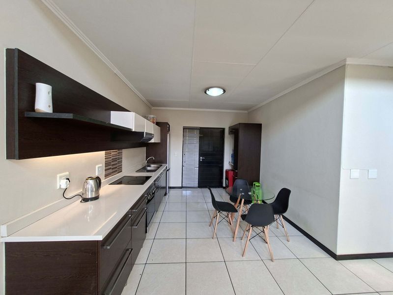 Modern open-plan kitchen featuring dark cabinetry, stone countertops, integrated appliances, and tiled flooring, seamlessly flowing into a dining area.