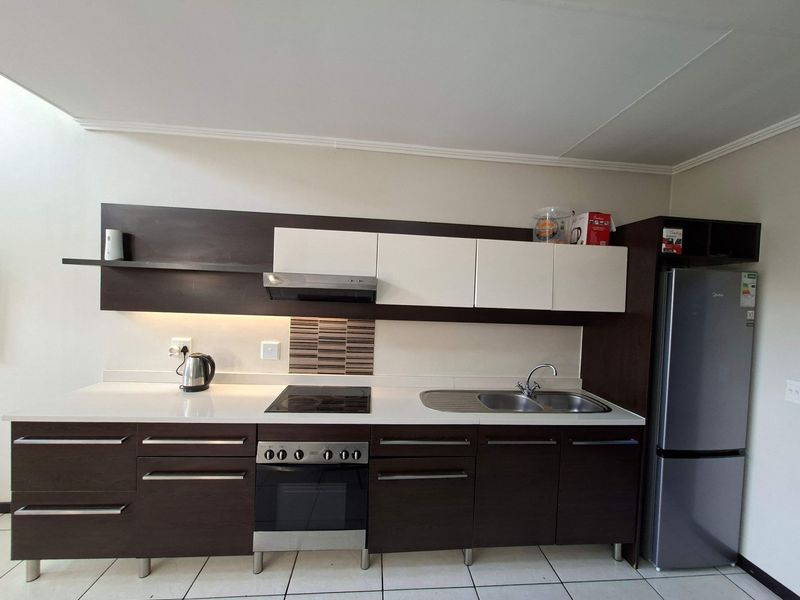 Modern kitchen featuring dark wood and white cabinetry, integrated electric hob, oven, extractor fan, and stainless steel sink with tiled flooring.