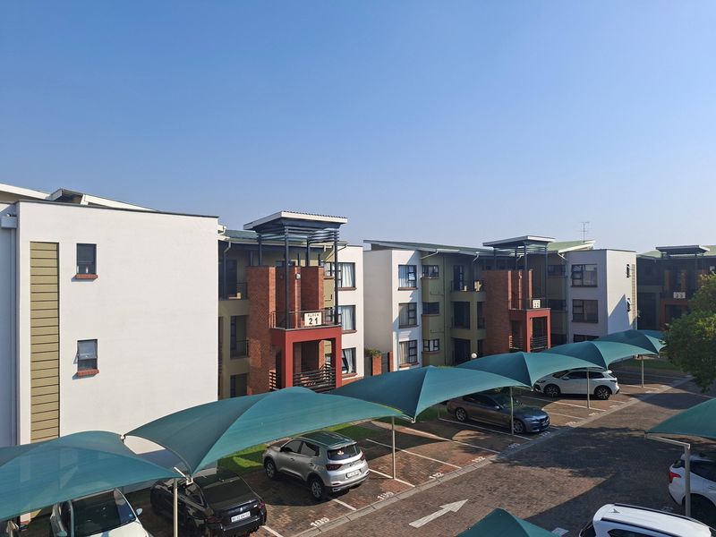 An elevated view of an apartment complex featuring paved parking areas with shade cloth carports and multi-story residential blocks with brick and plaster finishes.
