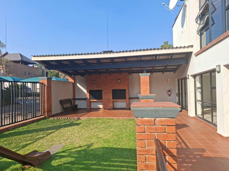 A spacious covered patio area featuring a built-in double braai, tiled flooring, and direct access to a private garden space.