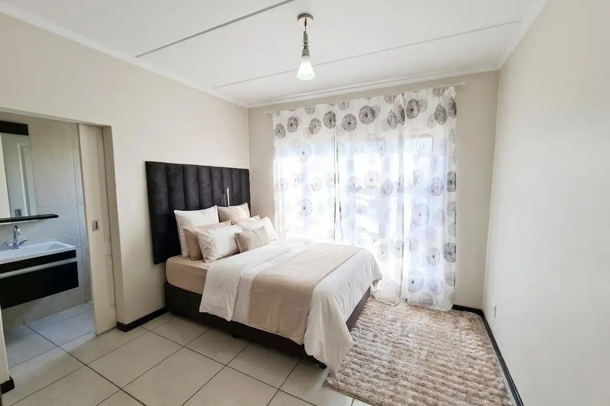 A well-lit bedroom featuring tiled flooring, a sliding door for natural light, and direct access to an en-suite bathroom.