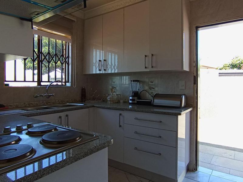 A functional kitchen featuring white gloss cabinetry, granite countertops, an integrated electric hob, and direct access to an outdoor area.