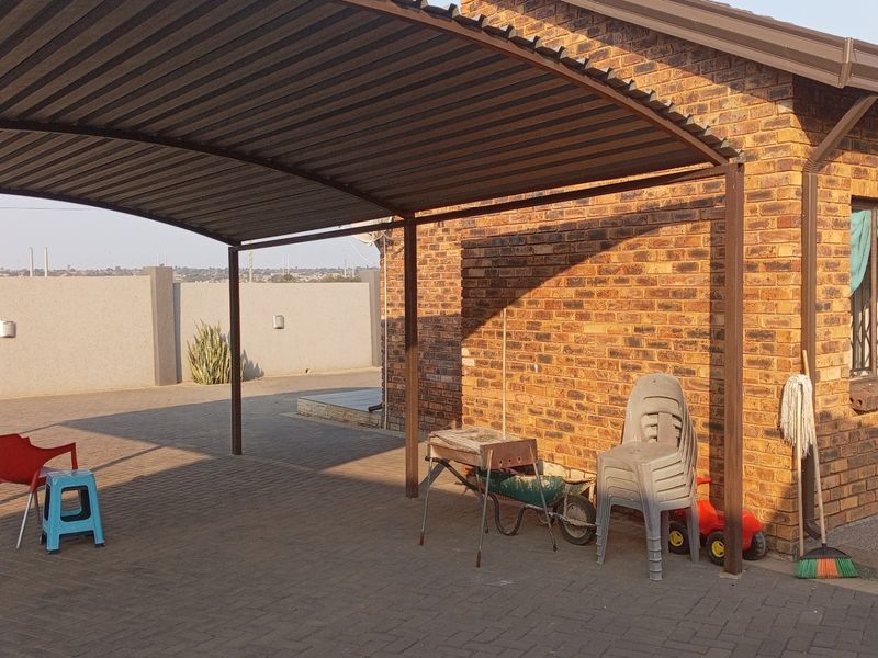 A covered outdoor patio area featuring a corrugated metal roof, brick exterior walls, and paved flooring, providing a functional space for outdoor activities.