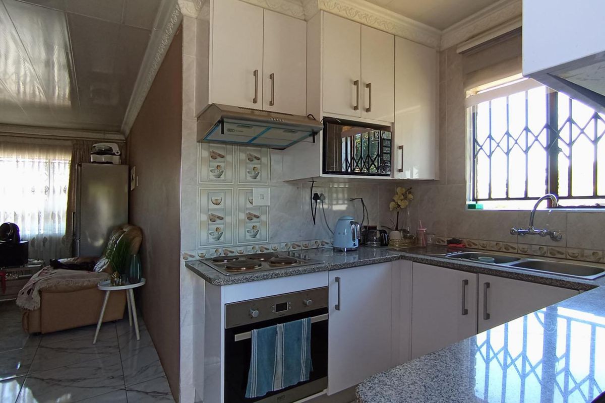 Compact kitchen featuring granite countertops, built-in oven, electric hob, extractor fan, and ample cabinetry, with an adjacent living area visible.