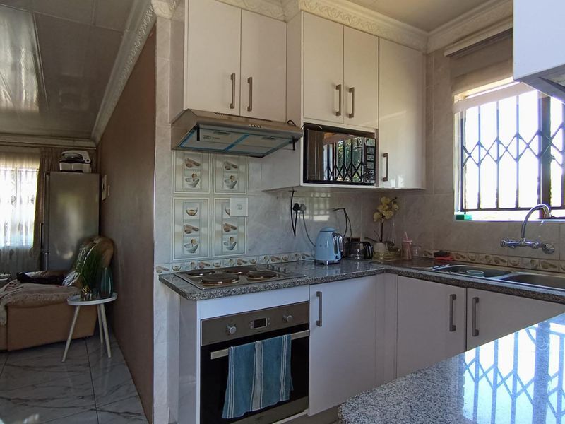 Compact kitchen featuring granite countertops, built-in oven, electric hob, extractor fan, and ample cabinetry, with an adjacent living area visible.