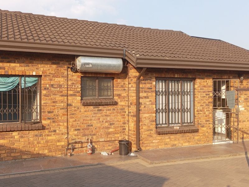 Rear view of a face brick house featuring a tiled roof, security gates on windows and doors, and a paved patio area.