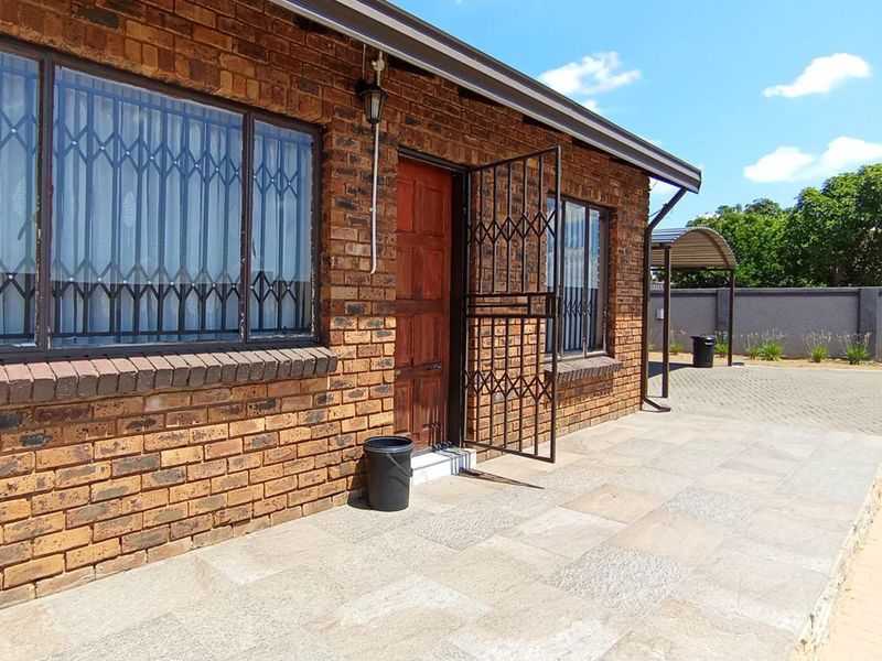 A face brick exterior front facade featuring a paved patio area, security gates on windows and doors, and a paved driveway.