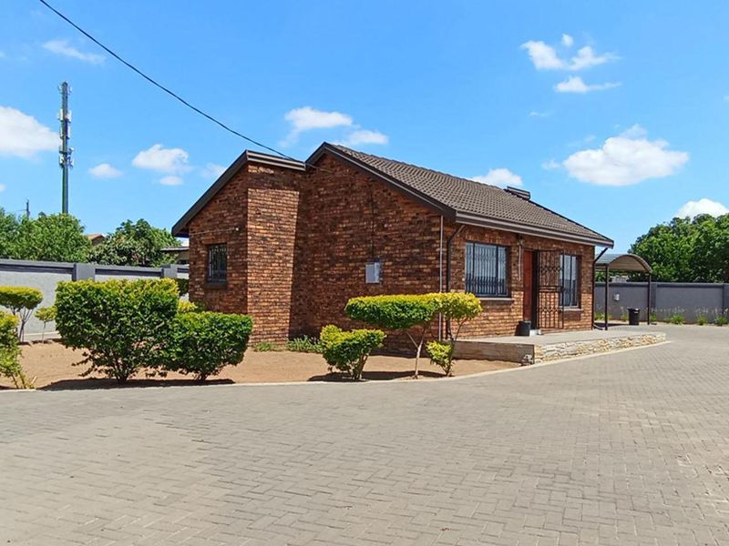 A well-maintained single-story face brick house featuring a paved driveway, secure window bars, and a neat perimeter wall.