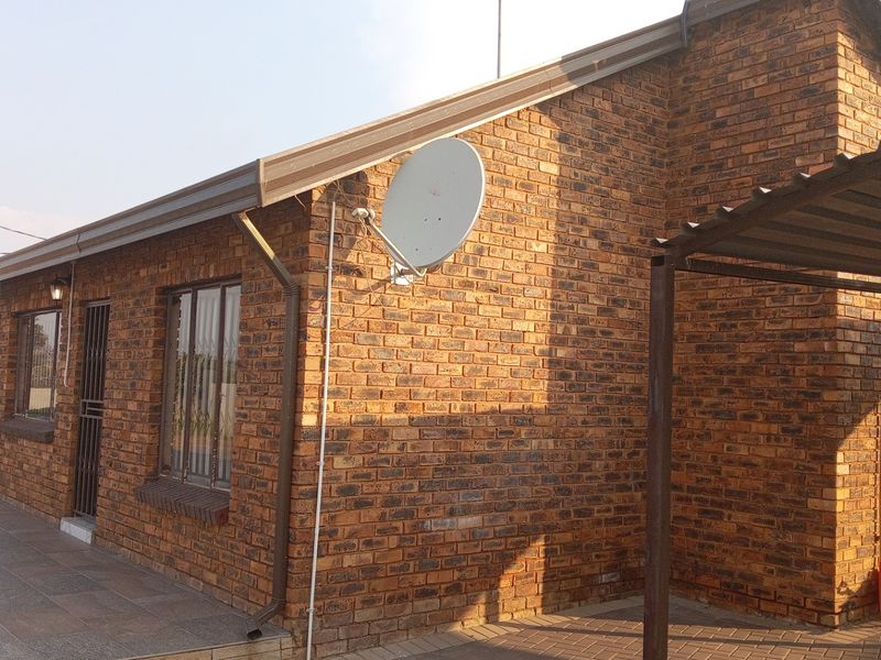 Exterior view of a face brick house featuring a tiled patio area, metal carport, and secure entrance.
