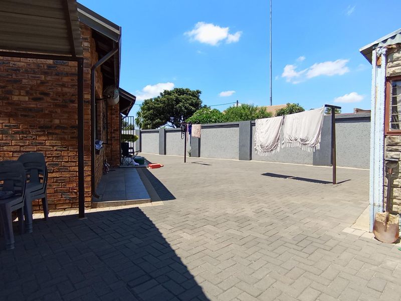 A spacious paved rear courtyard featuring a brick exterior wall, perimeter boundary wall, and a covered patio area.