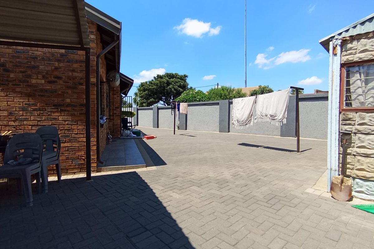 A spacious paved rear courtyard featuring a brick exterior wall, perimeter boundary wall, and a covered patio area.