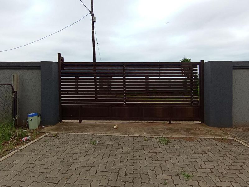Front view of the property featuring a modern slatted metal driveway gate, masonry boundary walls, and a paved driveway entrance.