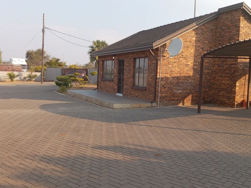 A well-maintained face brick house featuring a spacious paved driveway, a carport, and secure perimeter fencing.