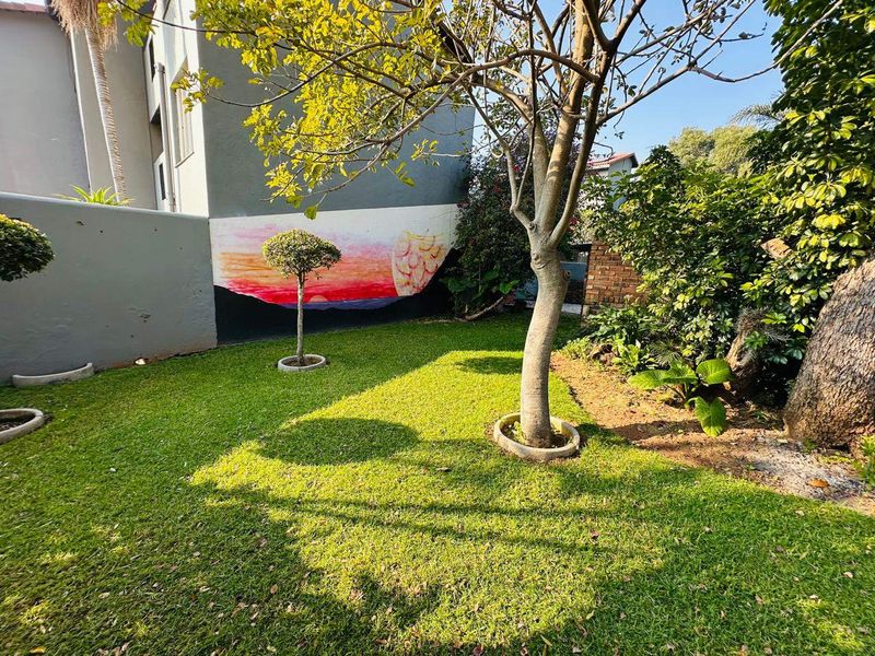 A private garden area featuring a well-maintained lawn, mature trees, and a decorative mural painted on the boundary wall.