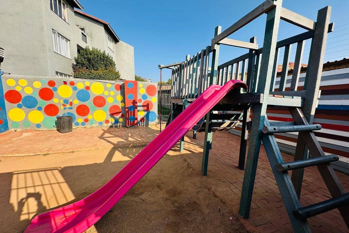 Outdoor communal area featuring a playground structure with a slide, set within a paved and sandy courtyard with decorative boundary walls.