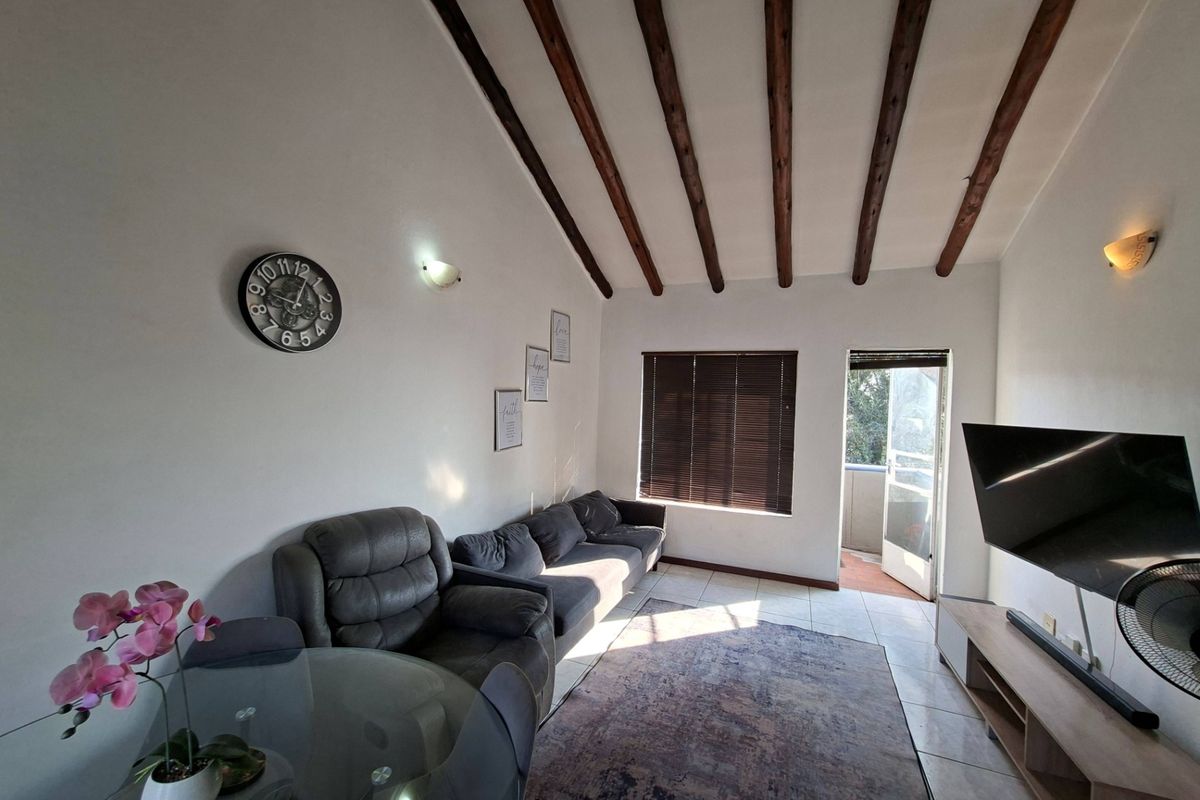 A living room featuring exposed timber ceiling beams, tiled flooring, and direct access to an outdoor balcony area.