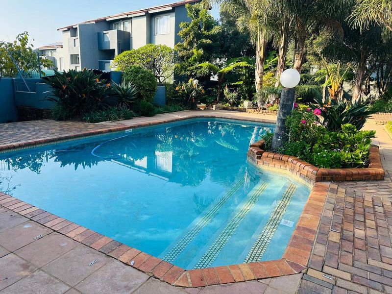 A well-maintained swimming pool area featuring brick paving, established garden landscaping, and a clear pool with integrated steps.