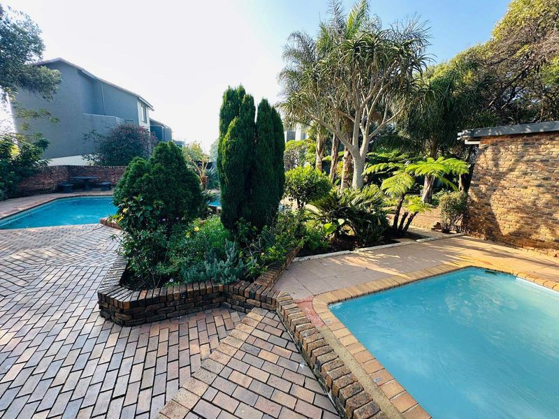 Outdoor pool area featuring a swimming pool, brick paving, and established garden landscaping with brick retaining walls.