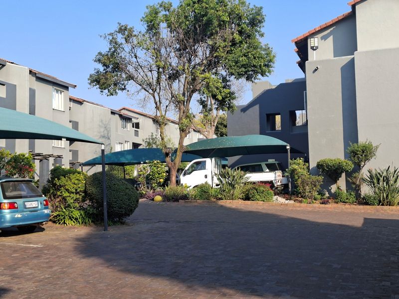 Exterior view of an apartment complex featuring paved parking areas with shade cloth carports and established garden landscaping.