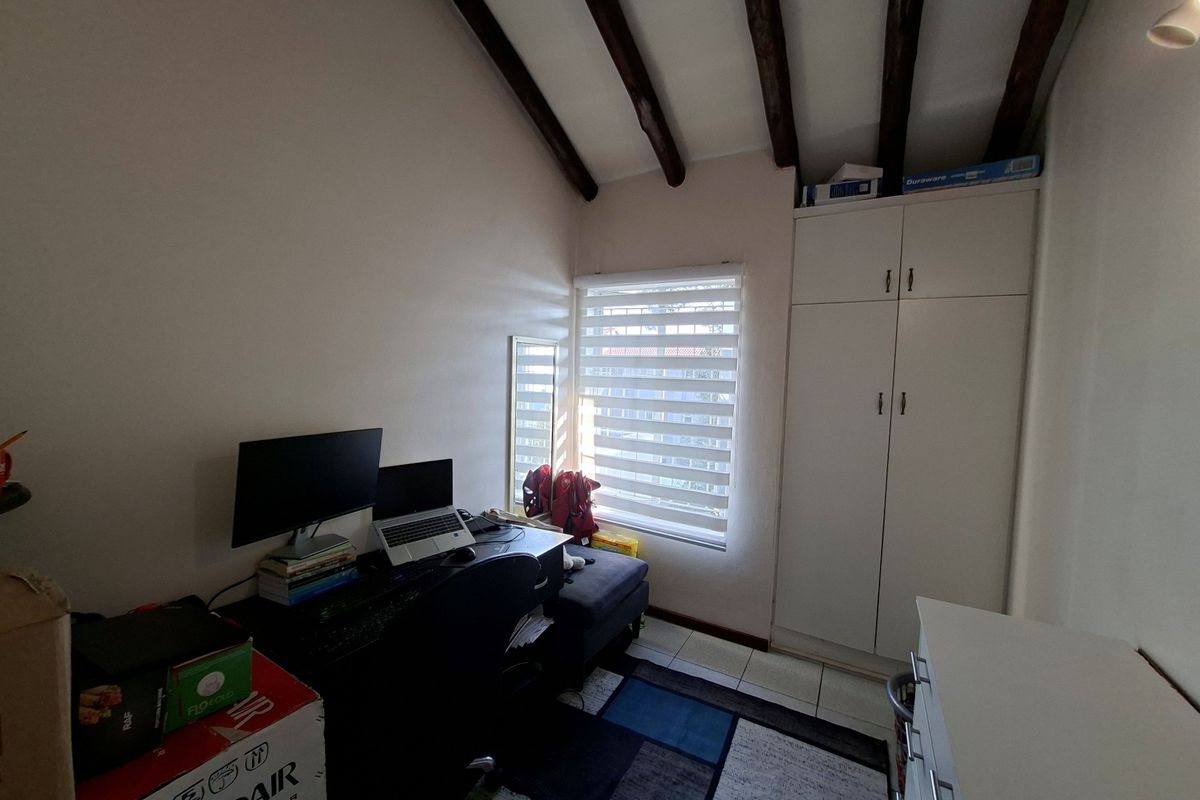 A bedroom featuring exposed timber ceiling beams, tiled flooring, and a built-in wardrobe, currently utilized as a home office space.