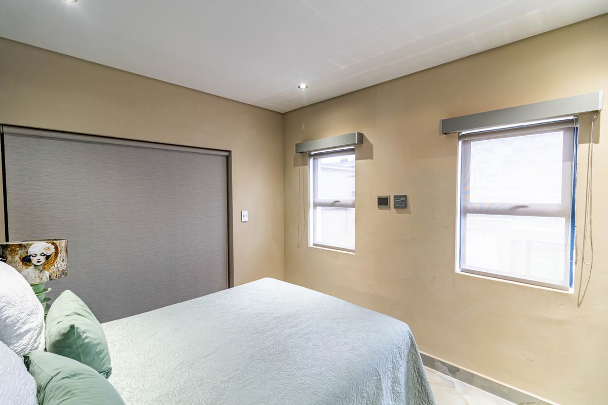 A bedroom featuring built-in cupboards, tiled flooring, and roller blinds on the windows, providing a functional and neutral living space.