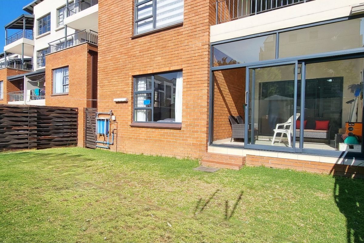 Rear view of the apartment featuring a private lawn area, brick exterior, and sliding glass doors leading into the living space.
