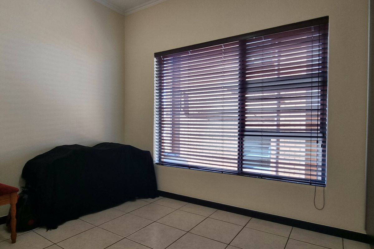 A spacious bedroom featuring neutral tiled flooring, built-in storage, and large windows fitted with venetian blinds.