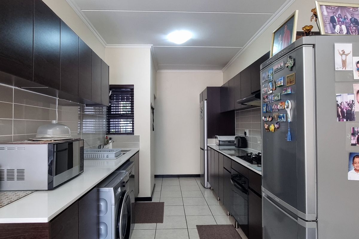 A functional galley-style kitchen featuring dark wood cabinetry, white stone countertops, tiled backsplash, and integrated appliances with ceramic floor tiles.