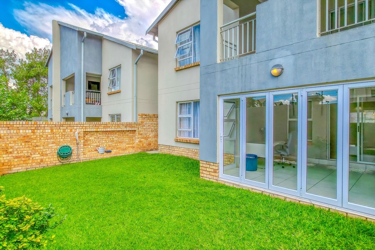 A private rear garden featuring a well-maintained lawn, brick boundary wall, and modern folding glass doors providing access to the interior living space.