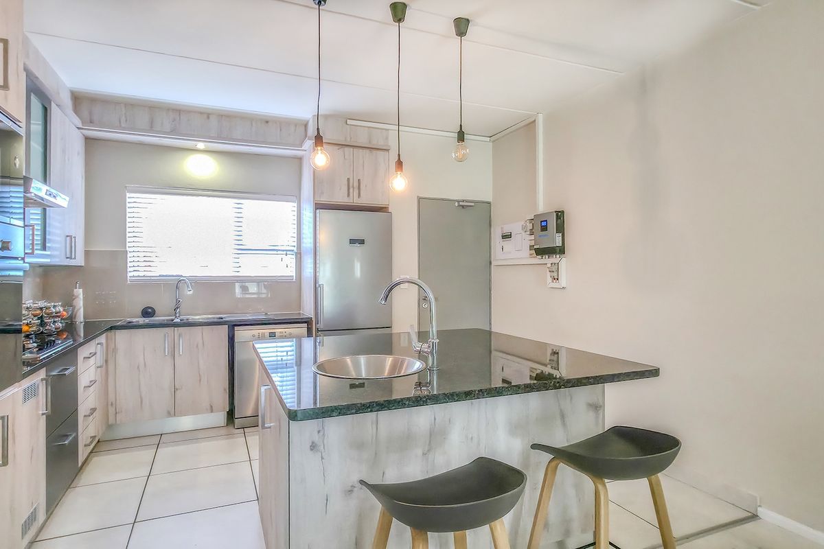 Modern kitchen featuring light wood-finish cabinetry, a central island with a stone countertop, built-in oven, and tiled flooring.