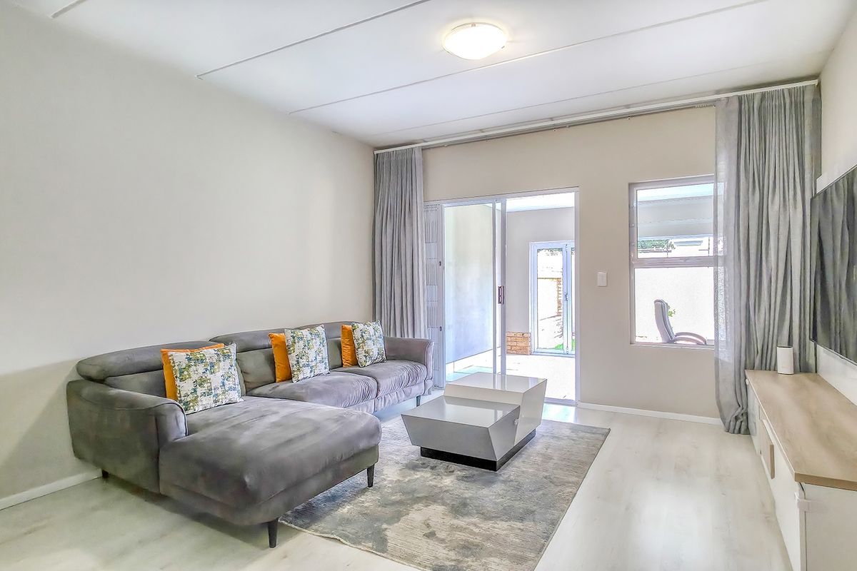 A bright and modern living room featuring laminate flooring, neutral walls, and a sliding glass door providing access to an outdoor patio area.