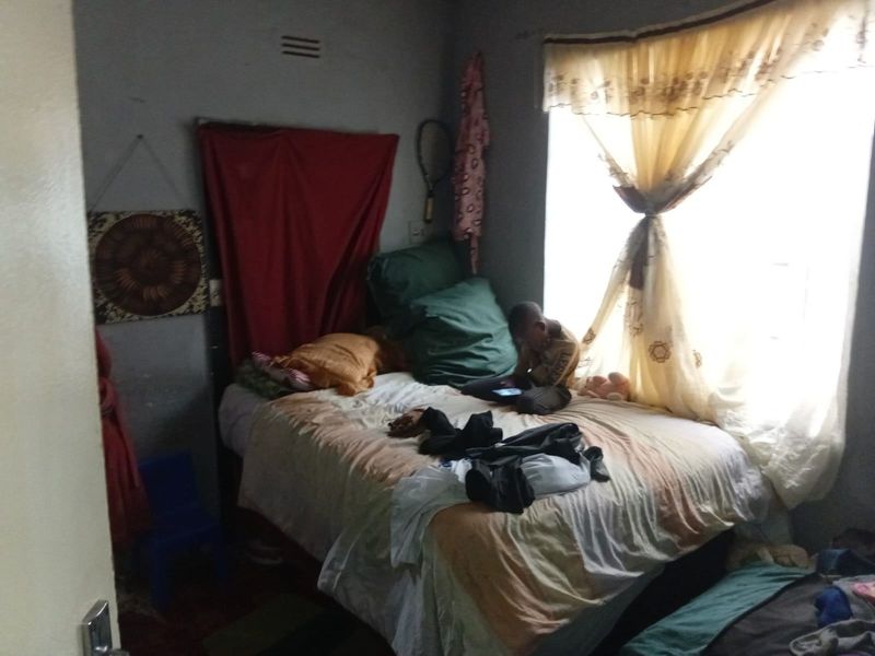 A compact bedroom featuring a window with curtains and basic wall finishes, suitable for renovation to improve the overall aesthetic and functionality.