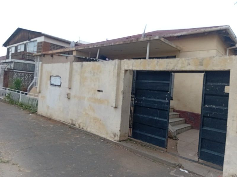 Front exterior view of a residential property featuring a boundary wall, metal gate, and a covered entrance porch with concrete steps.