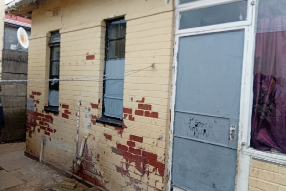 Rear exterior view of the property showing brick facade with significant paint peeling and wear, requiring maintenance and exterior refurbishment.
