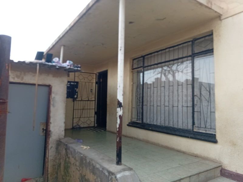 Front entrance area featuring a tiled porch, security gate, and security bars on the window, showing signs of significant wear and weathering.