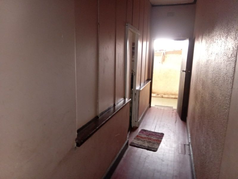A narrow hallway featuring timber flooring and a dado rail, leading towards an external doorway.