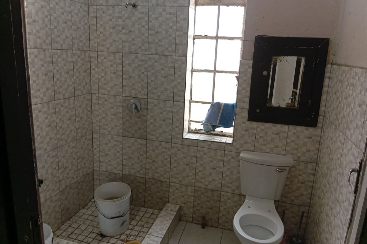 A compact bathroom featuring a tiled shower area, standard toilet, and steel-framed window, requiring renovation to update finishes and fixtures.