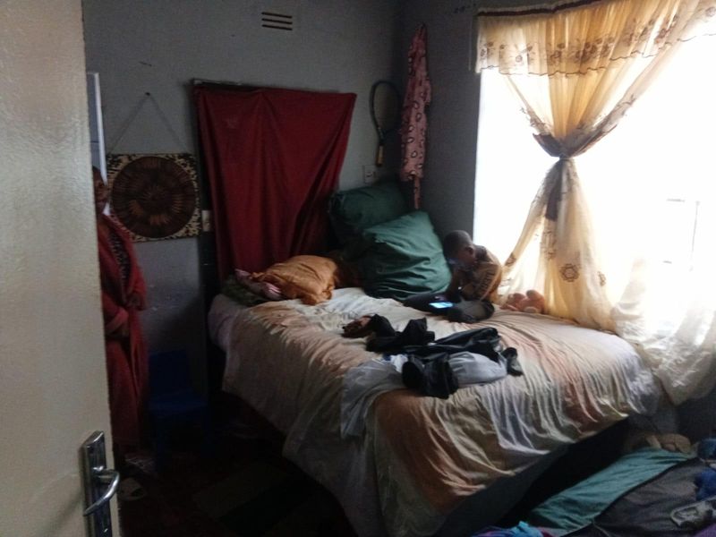 A bedroom featuring a window with curtains and a door, showing signs of wear and dated finishes.