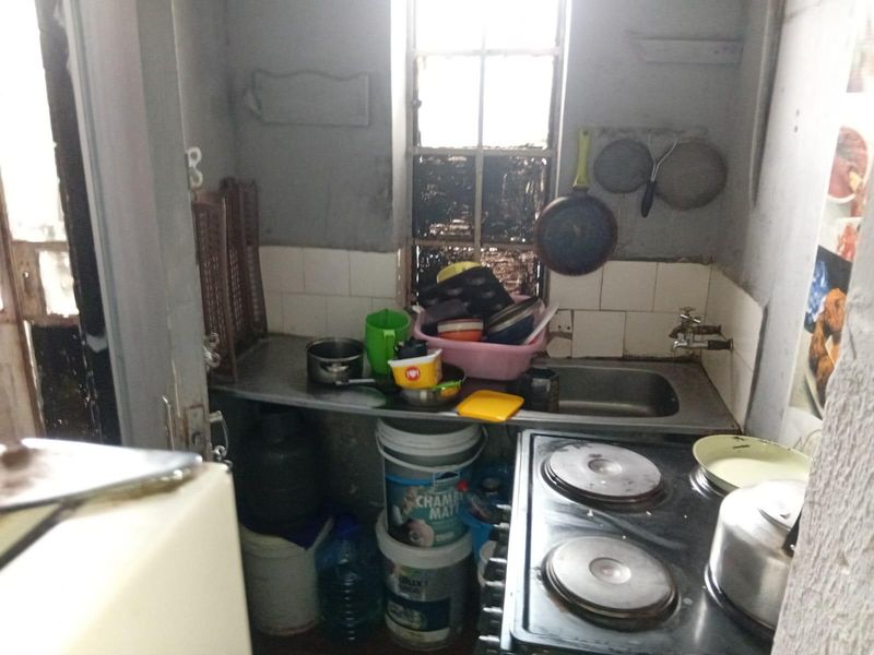 A compact kitchen area featuring a stainless steel sink, tiled splashback, and electric hob, requiring significant cosmetic updates and maintenance.