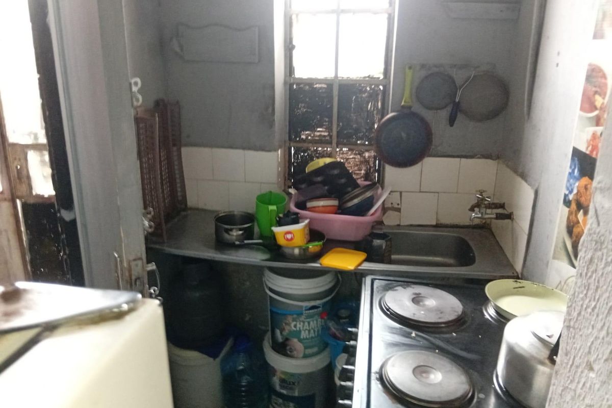 A compact kitchen area featuring a stainless steel sink, tiled splashback, and electric hob, requiring significant cosmetic updates and maintenance.