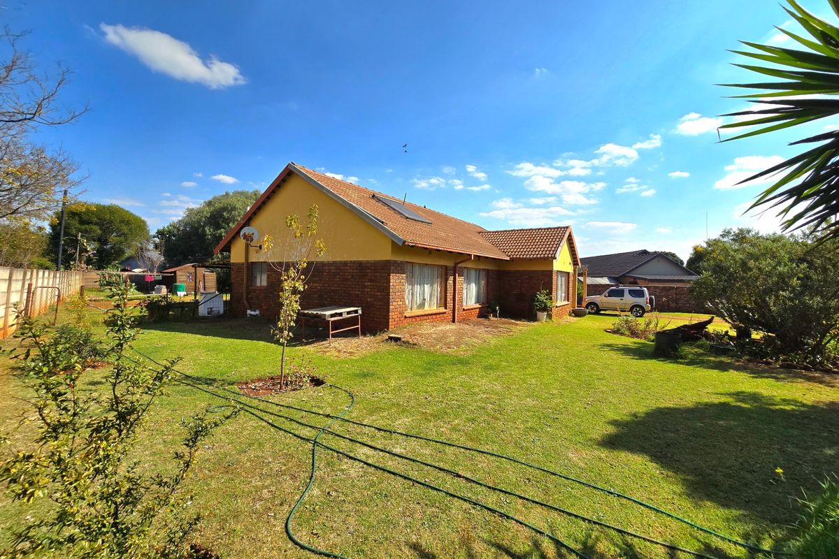 Rear view of a single-story brick house featuring a tiled roof, solar water heater, and a spacious garden area.