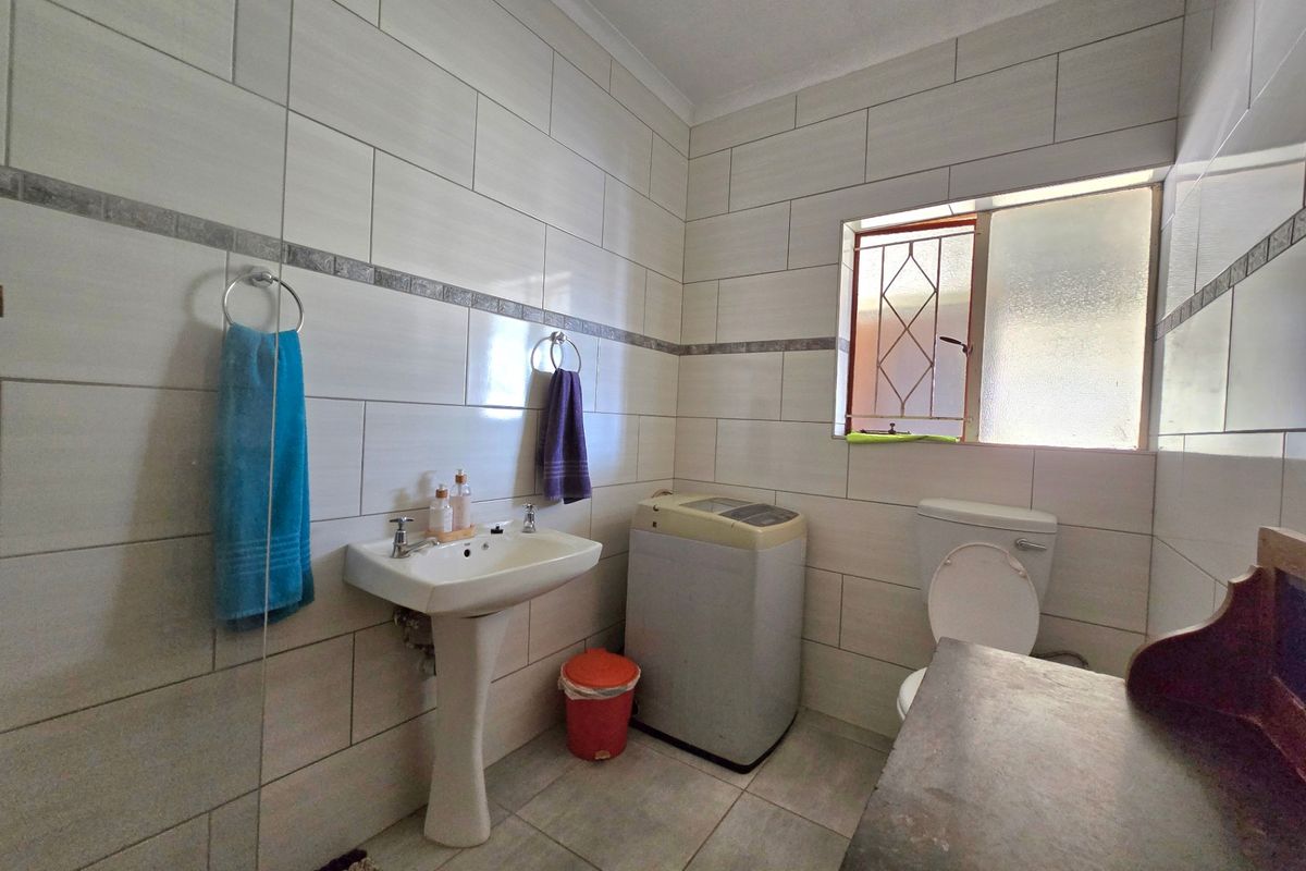 A functional bathroom featuring tiled walls and flooring, equipped with a pedestal washbasin and a standard toilet.